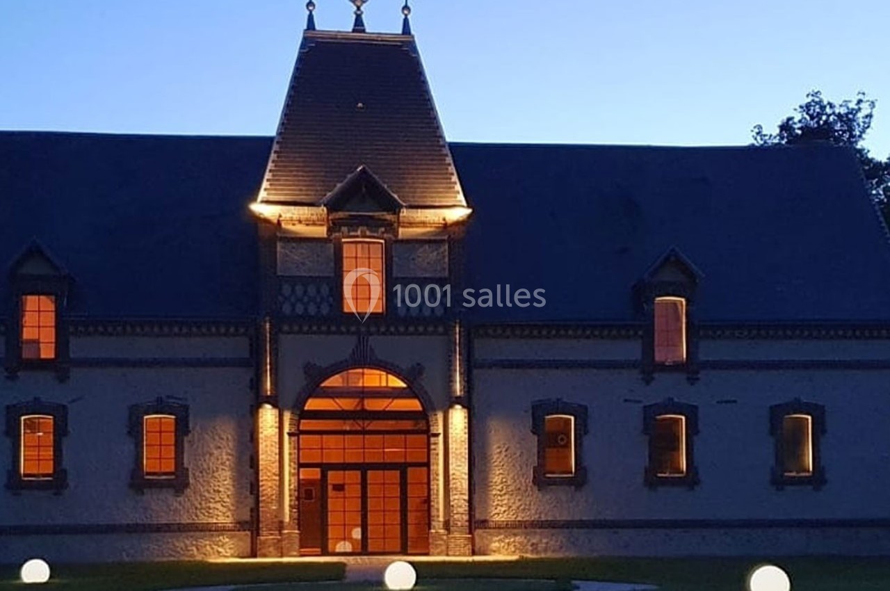 Façade d'un bâtiment ancien éclairé à la tombée de la nuit, avec des lumières rondes sur la pelouse.