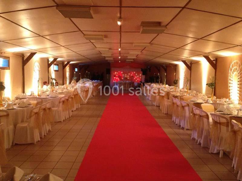 Salle de réception décorée avec des tables dressées de chaque côté d'un tapis rouge central.