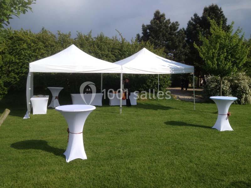 Tentes blanches installées sur une pelouse avec des tables hautes recouvertes de nappes blanches.