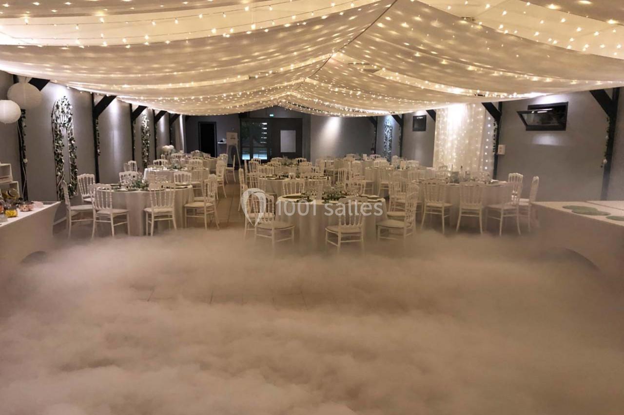 Salle de réception décorée avec des guirlandes lumineuses, des tables dressées et un effet de fumée au sol.