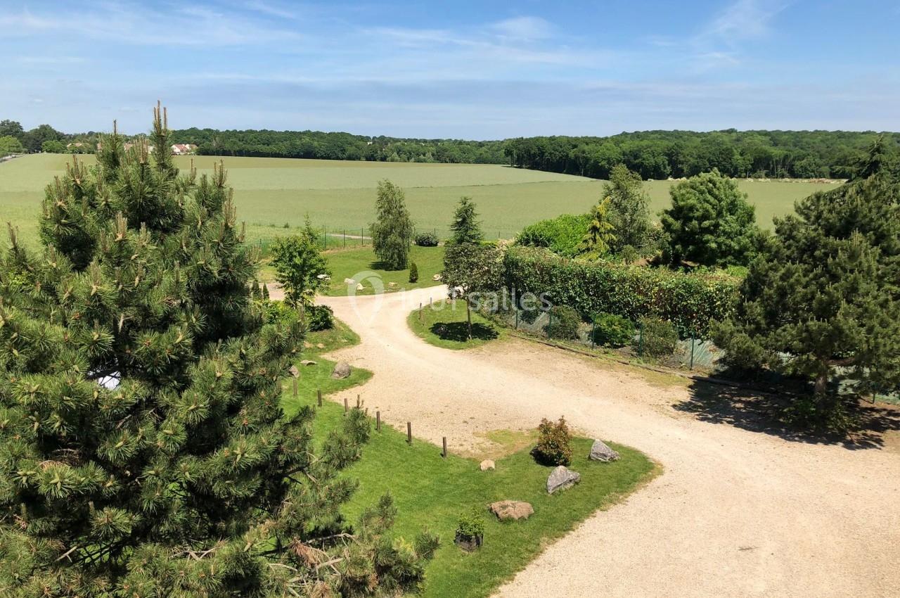 Chemin de gravier sinueux traversant un paysage verdoyant avec arbres, pelouses et champs sous un ciel bleu.