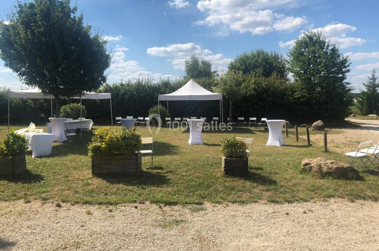 Espace extérieur aménagé avec des tentes, tables et chaises sur une pelouse, entouré de verdure sous un ciel dégagé.