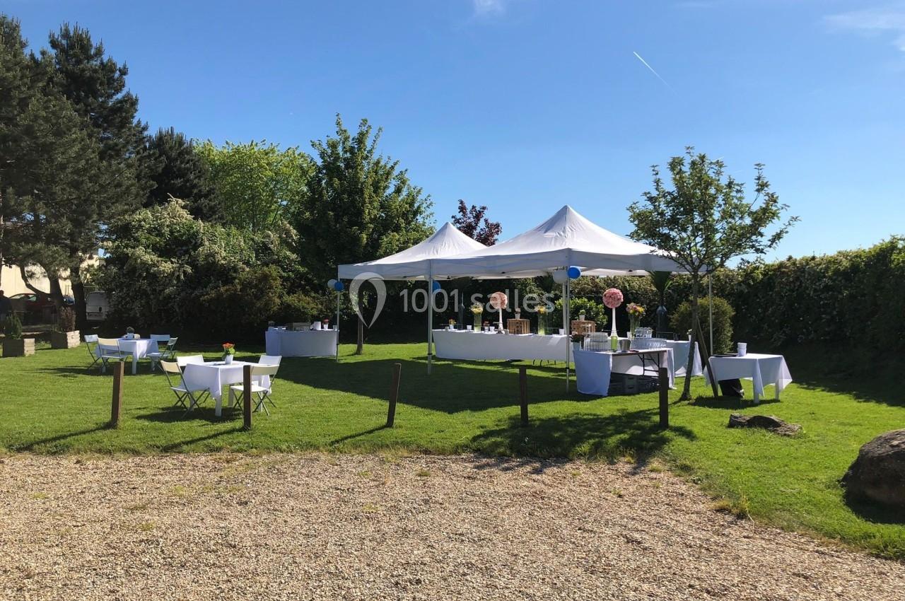 Tentes blanches installées sur une pelouse avec des tables décorées pour un événement en extérieur par temps ensoleillé.
