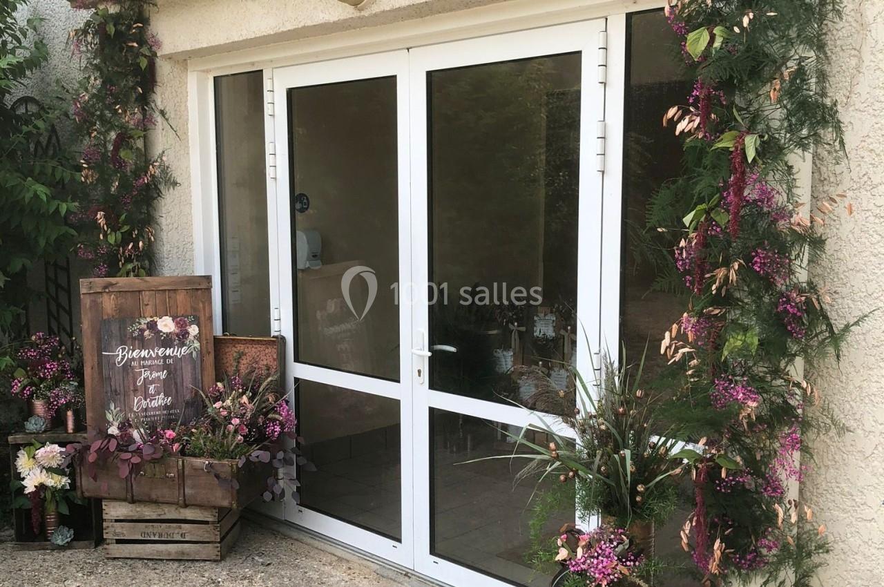 Entrée vitrée décorée de guirlandes florales et d'un panneau en bois entouré de fleurs.