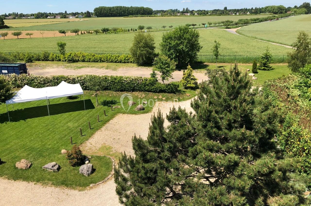 Vue aérienne d'un jardin avec pelouse, arbres, tente blanche et champs verdoyants à l'arrière-plan.