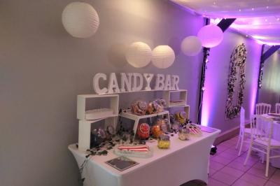 Table de candy bar décorée avec des bonbons variés, lanternes suspendues et éclairage violet en arrière-plan.
