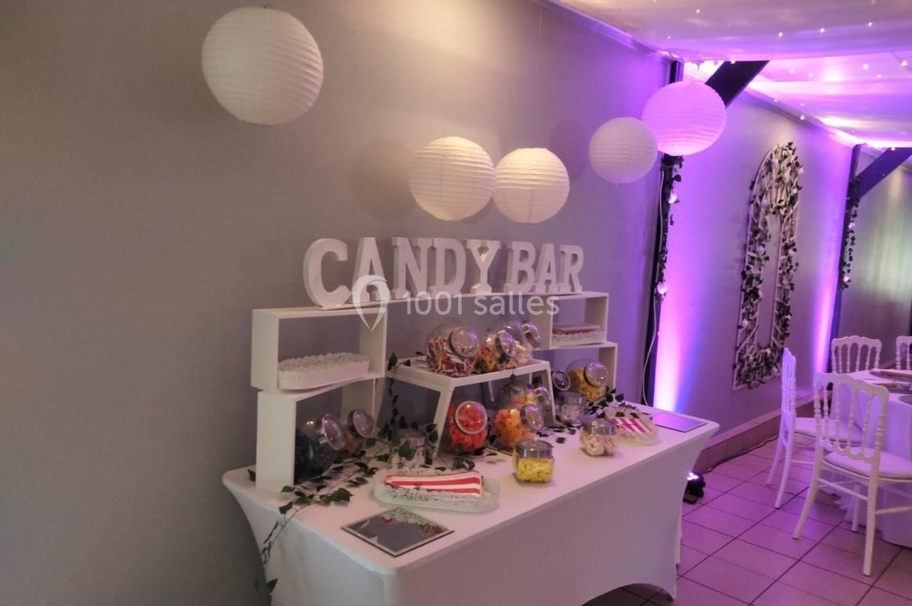Table de candy bar décorée avec des bonbons variés, lanternes suspendues et éclairage violet en arrière-plan.