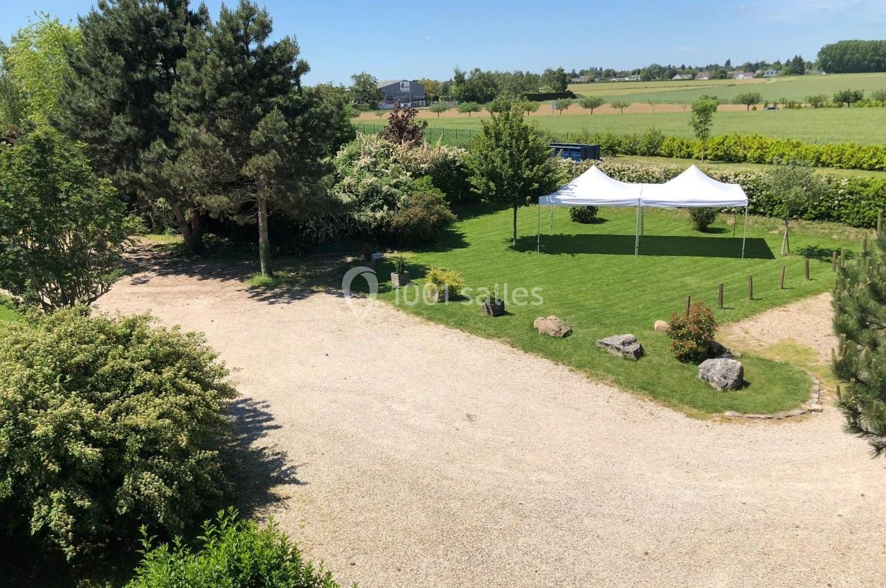 Vue d'un jardin avec pelouse, arbres, allée gravillonnée et deux tentes blanches installées sur le gazon.