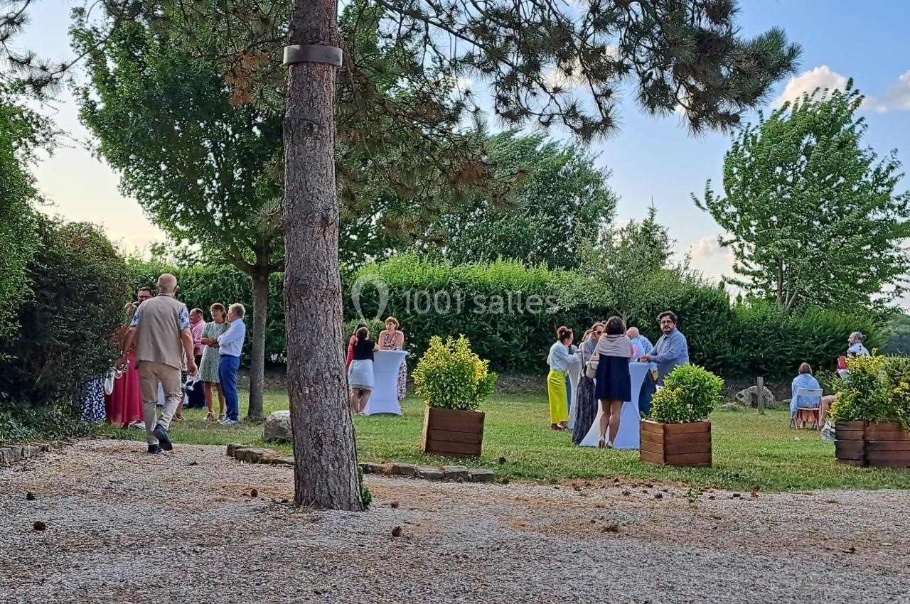 Groupe de personnes discutant debout dans un jardin arboré par une journée ensoleillée.