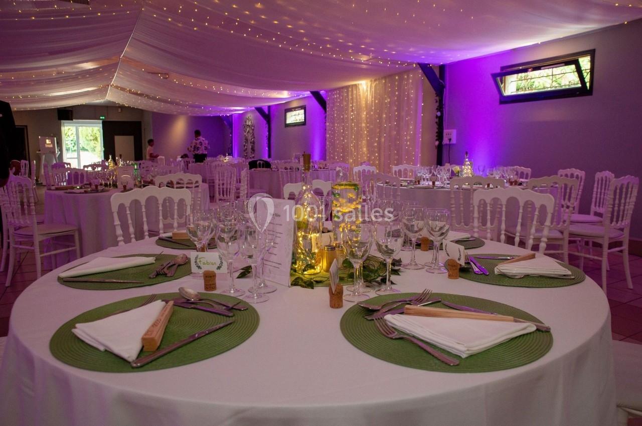 Salle de réception décorée avec des tables rondes dressées, éclairage tamisé et guirlandes lumineuses au plafond.