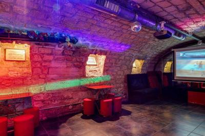 Bar avec comptoir rouge éclairé, tabourets hauts, murs en pierre et briques, décorations murales et étagères avec bouteilles.