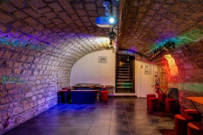 Bar avec comptoir rouge éclairé, tabourets hauts, murs en pierre et briques, décorations murales et étagères avec bouteilles.