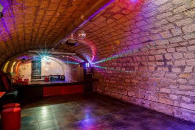 Bar avec comptoir rouge éclairé, tabourets hauts, murs en pierre et briques, décorations murales et étagères avec bouteilles.