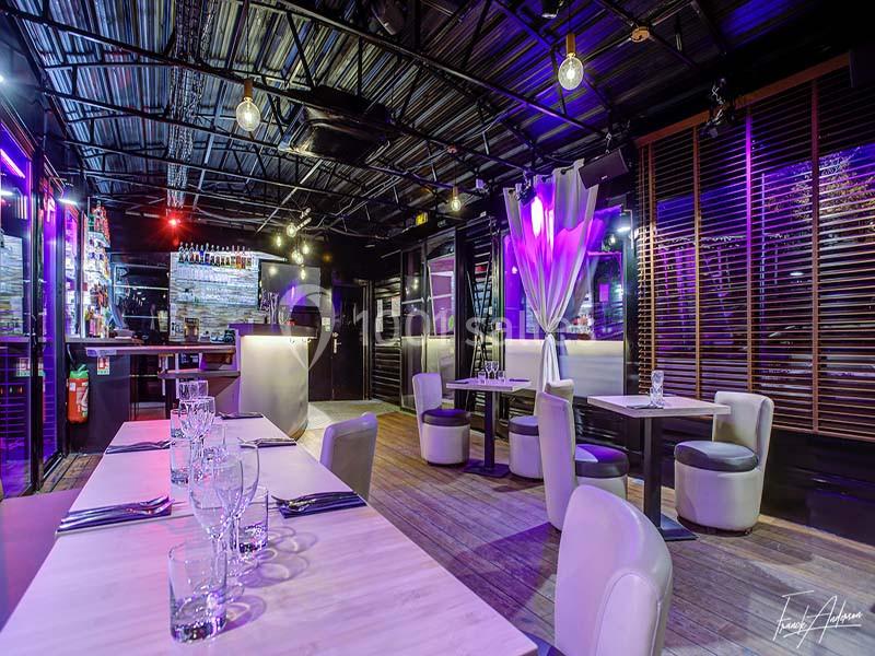 Salle de restaurant moderne avec éclairage coloré, tables dressées et décor contemporain.