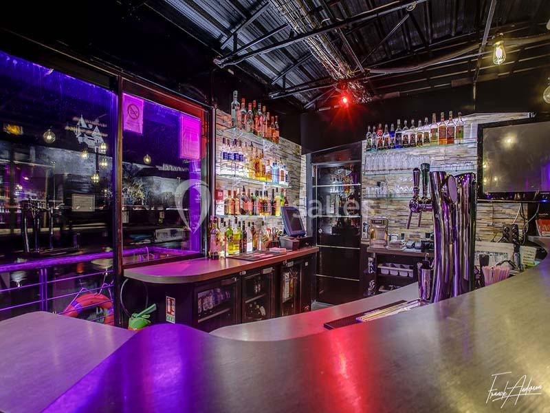 Bar moderne avec comptoir incurvé, étagères remplies de bouteilles, lumières colorées et ambiance nocturne.