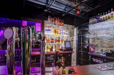 Bar moderne avec comptoir éclairé, bouteilles en arrière-plan, trois verres et une bouteille de champagne au premier plan.