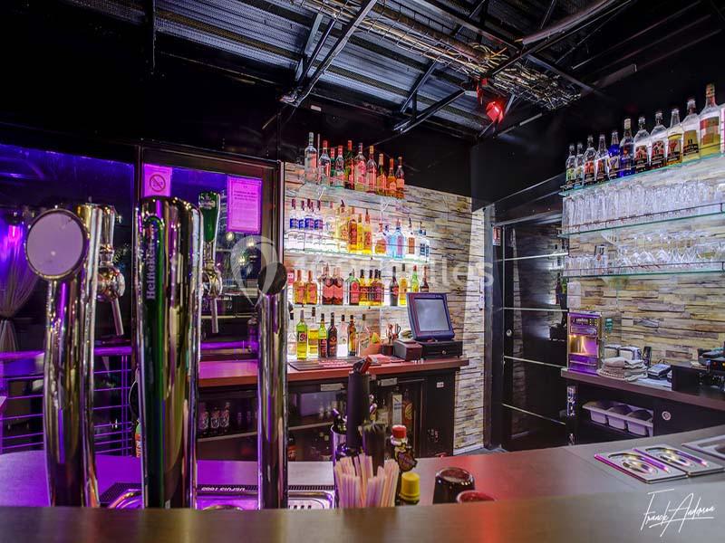 Comptoir de bar moderne avec tireuses à bière, étagères de bouteilles illuminées et caisse enregistreuse.