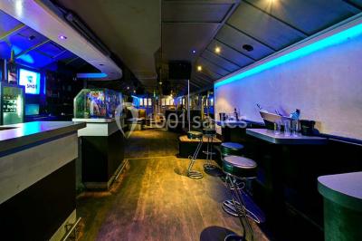 Bar moderne avec comptoir éclairé, bouteilles en arrière-plan, trois verres et une bouteille de champagne au premier plan.