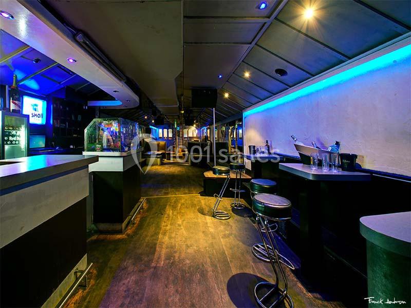 Intérieur d'un bar avec comptoir, tabourets hauts, éclairage tamisé et néons bleus.