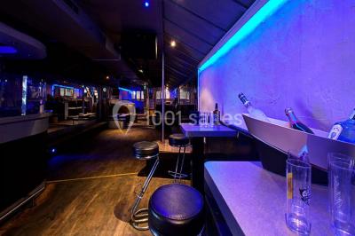 Bar moderne avec comptoir éclairé, bouteilles en arrière-plan, trois verres et une bouteille de champagne au premier plan.