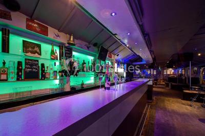 Bar moderne avec comptoir éclairé, bouteilles en arrière-plan, trois verres et une bouteille de champagne au premier plan.