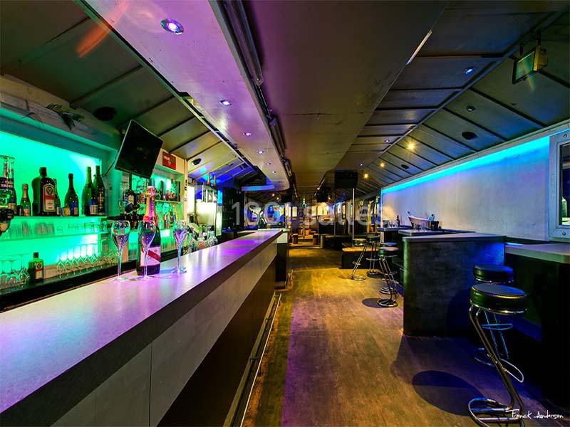 Intérieur d'un bar moderne avec comptoir éclairé, tabourets hauts et éclairage coloré.