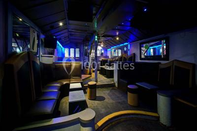 Bar moderne avec comptoir éclairé, bouteilles en arrière-plan, trois verres et une bouteille de champagne au premier plan.