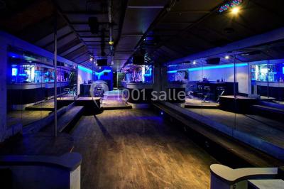 Bar moderne avec comptoir éclairé, bouteilles en arrière-plan, trois verres et une bouteille de champagne au premier plan.