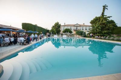 Vue d'une terrasse avec parasols et piscine, encadrée par des haies sombres et un ciel dégagé en arrière-plan.