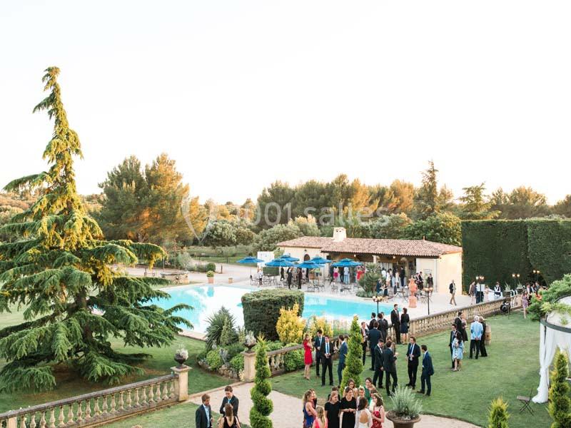 Vue d'un jardin avec piscine, invités en tenue de soirée rassemblés pour un événement en plein air au coucher du soleil.