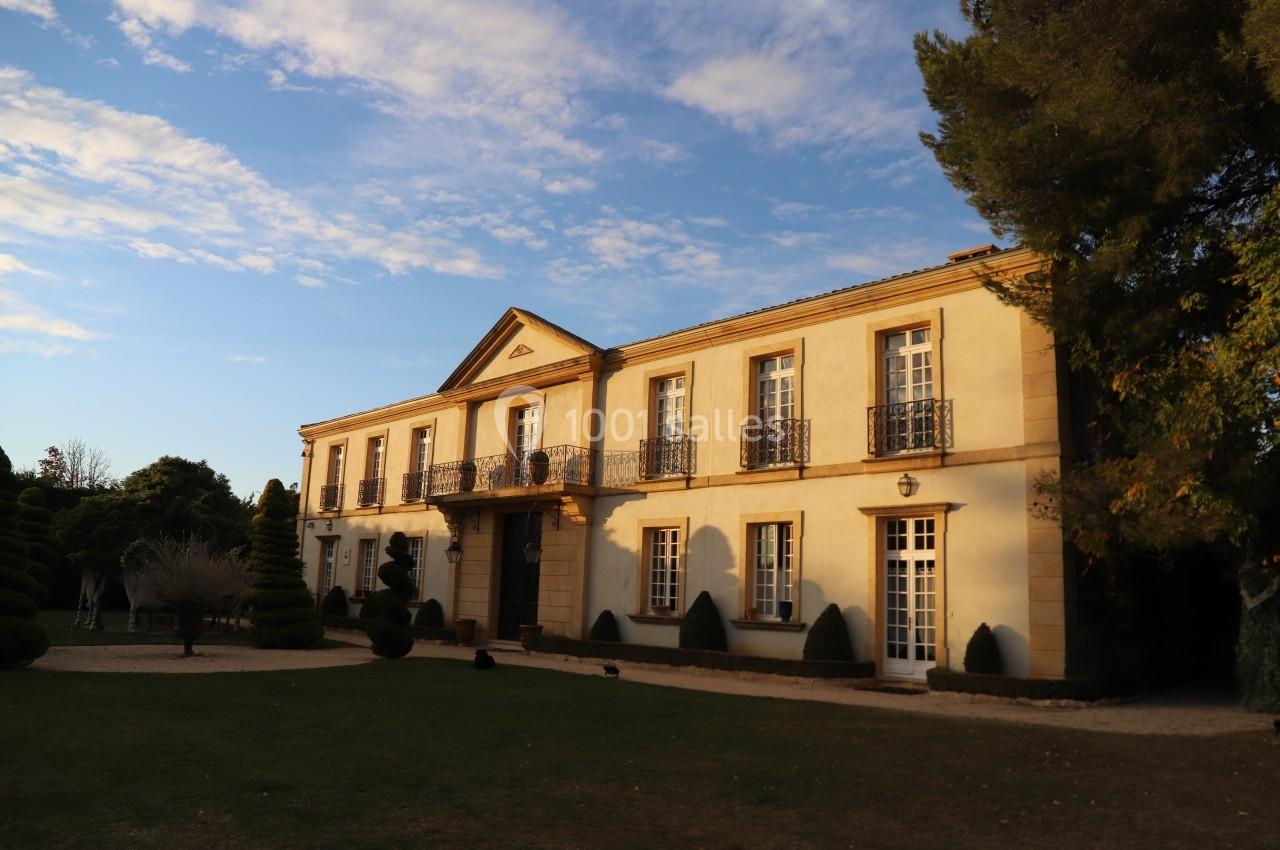 Façade d'une grande maison de style classique avec jardin, éclairée par une lumière douce en fin de journée.