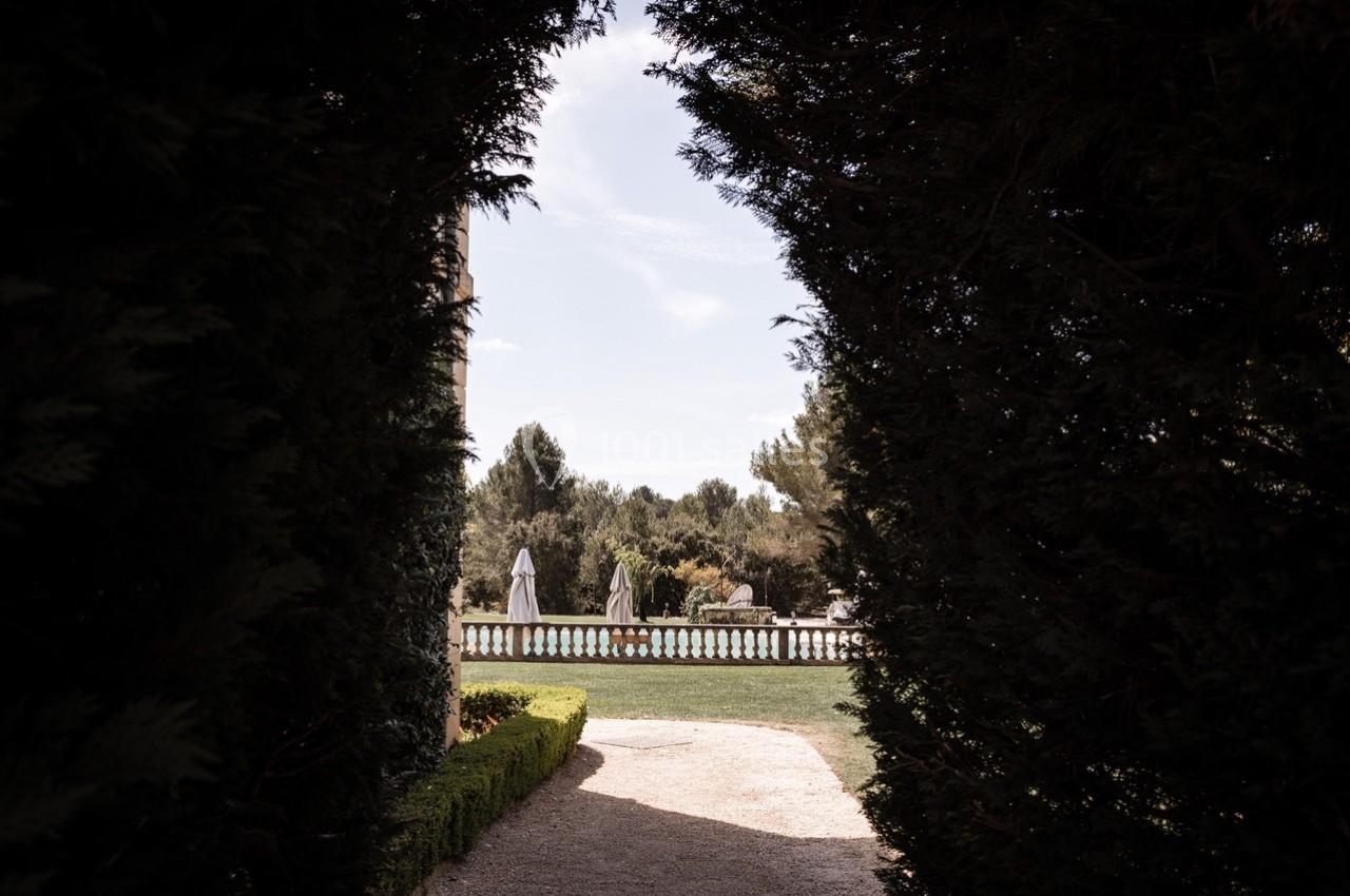 Vue d'une terrasse avec parasols et piscine, encadrée par des haies sombres et un ciel dégagé en arrière-plan.