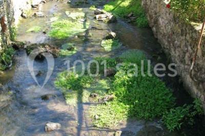 Petit ruisseau bordé de végétation avec des tentes blanches installées pour un événement en arrière-plan.