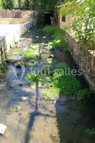 Ruisseau peu profond bordé de murs en pierre, avec végétation et ombres d'arbres sur l'eau.