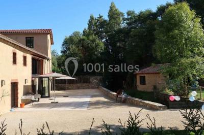 Petit ruisseau bordé de végétation avec des tentes blanches installées pour un événement en arrière-plan.