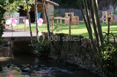 Petit ruisseau bordé de végétation avec des tentes blanches installées pour un événement en arrière-plan.