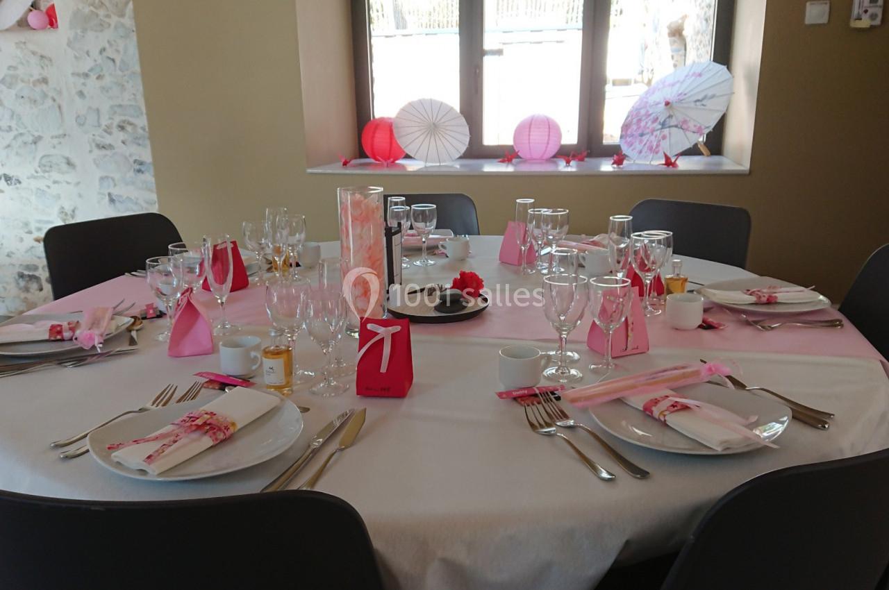 Table ronde décorée pour un événement, avec nappes blanches, serviettes roses, vaisselle et décorations élégantes.