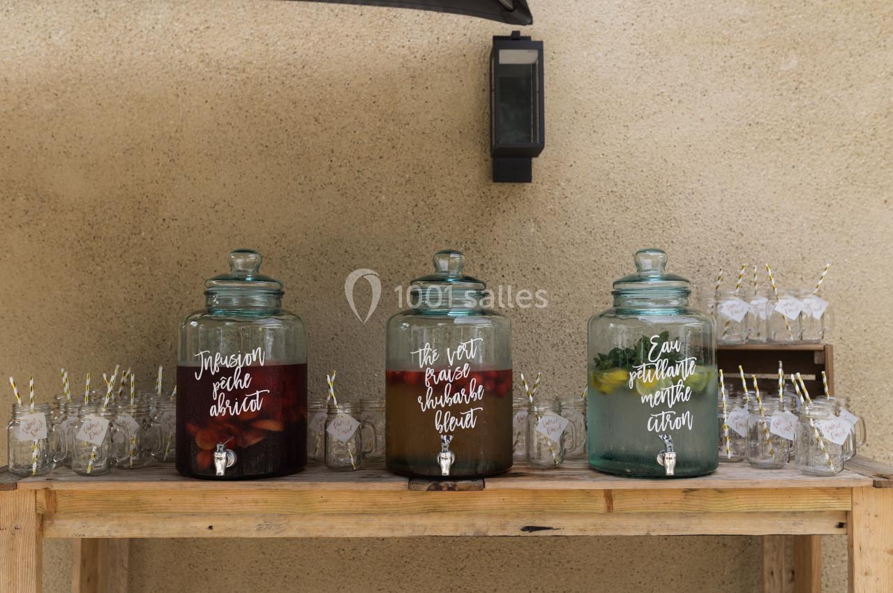 Trois distributeurs en verre contenant des boissons aromatisées, posés sur une table en bois avec des verres et pailles.