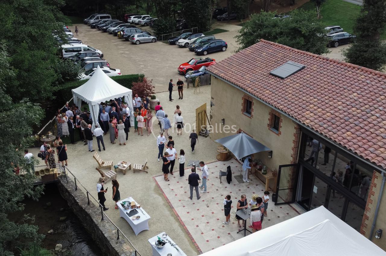 Vue aérienne d'un événement en plein air avec des invités rassemblés près d'une bâtisse et de tentes blanches.