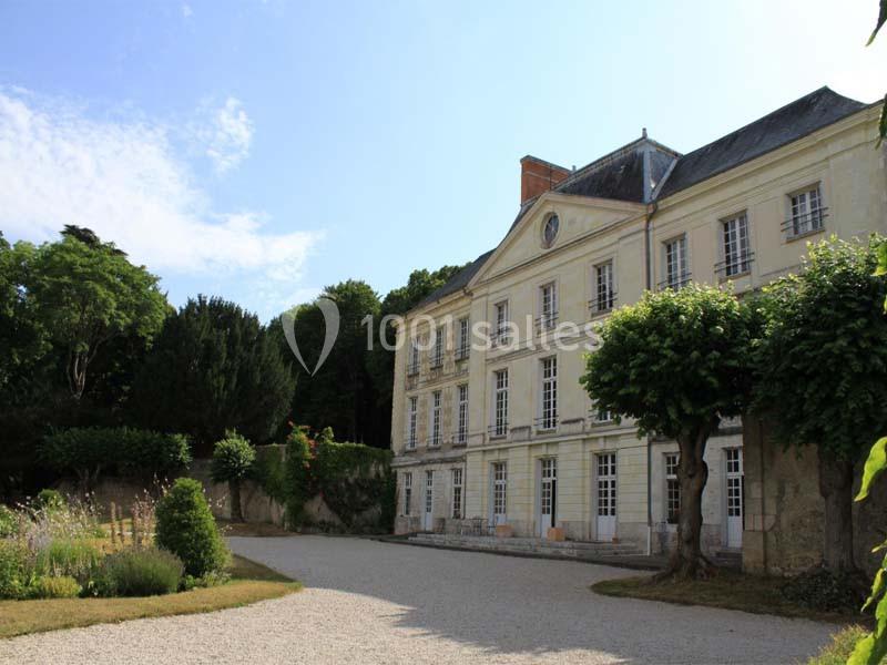 Façade d'un bâtiment ancien entouré d'arbres et d'un jardin, avec une allée gravillonnée au premier plan.