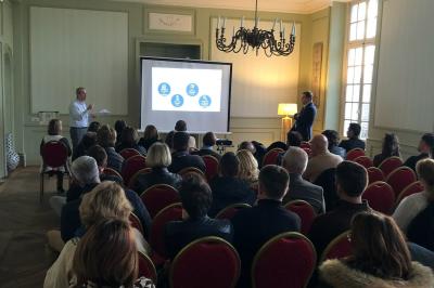 Écran de projection blanc déroulé dans une salle de conférence avec murs en bois et plafond équipé d'un projecteur.