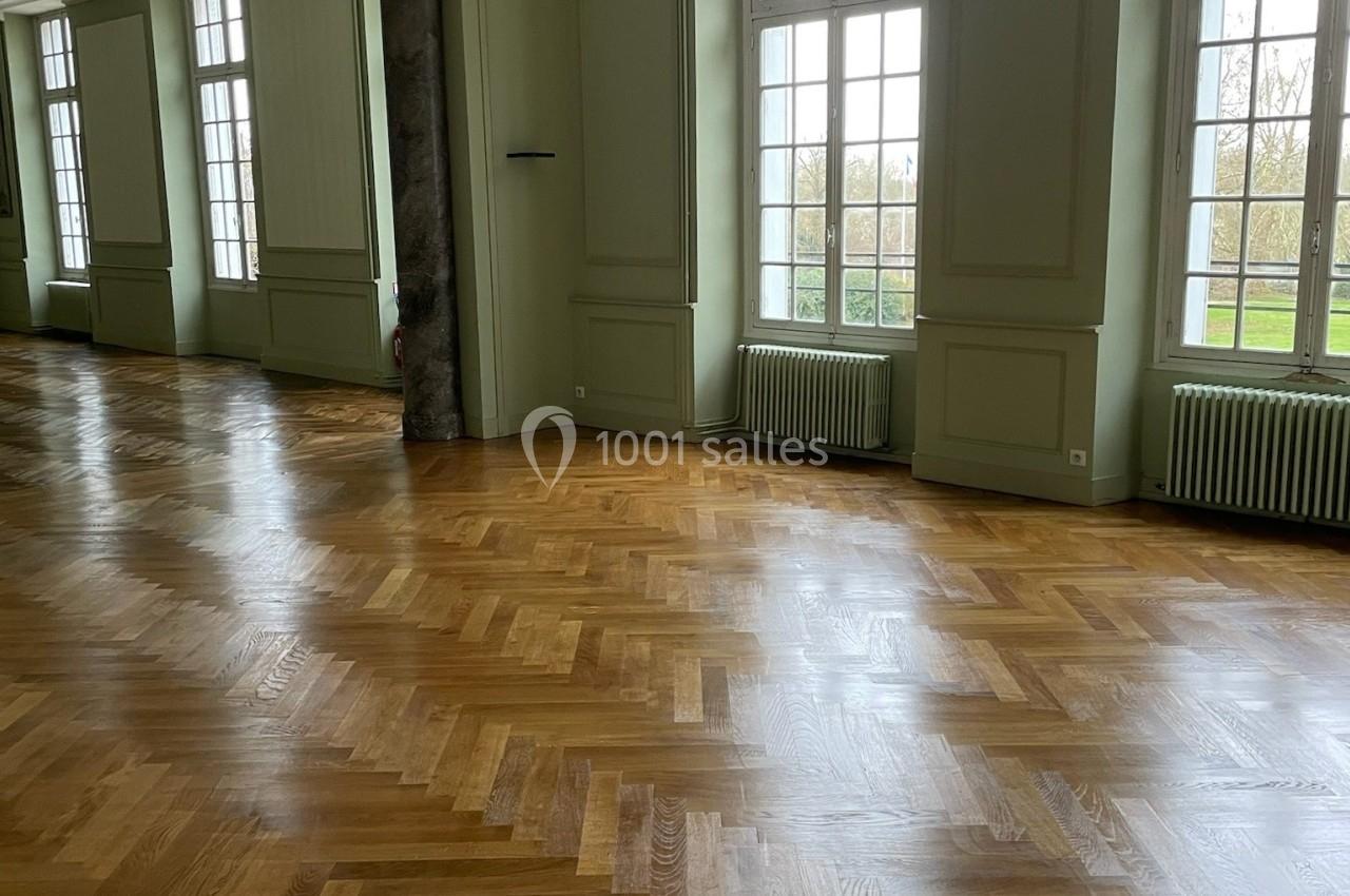 Salle lumineuse avec parquet en chevrons, grandes fenêtres donnant sur un extérieur verdoyant.