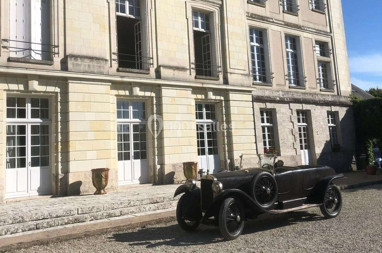 Voiture ancienne noire stationnée devant un bâtiment en pierre avec de grandes fenêtres et des jardinières.