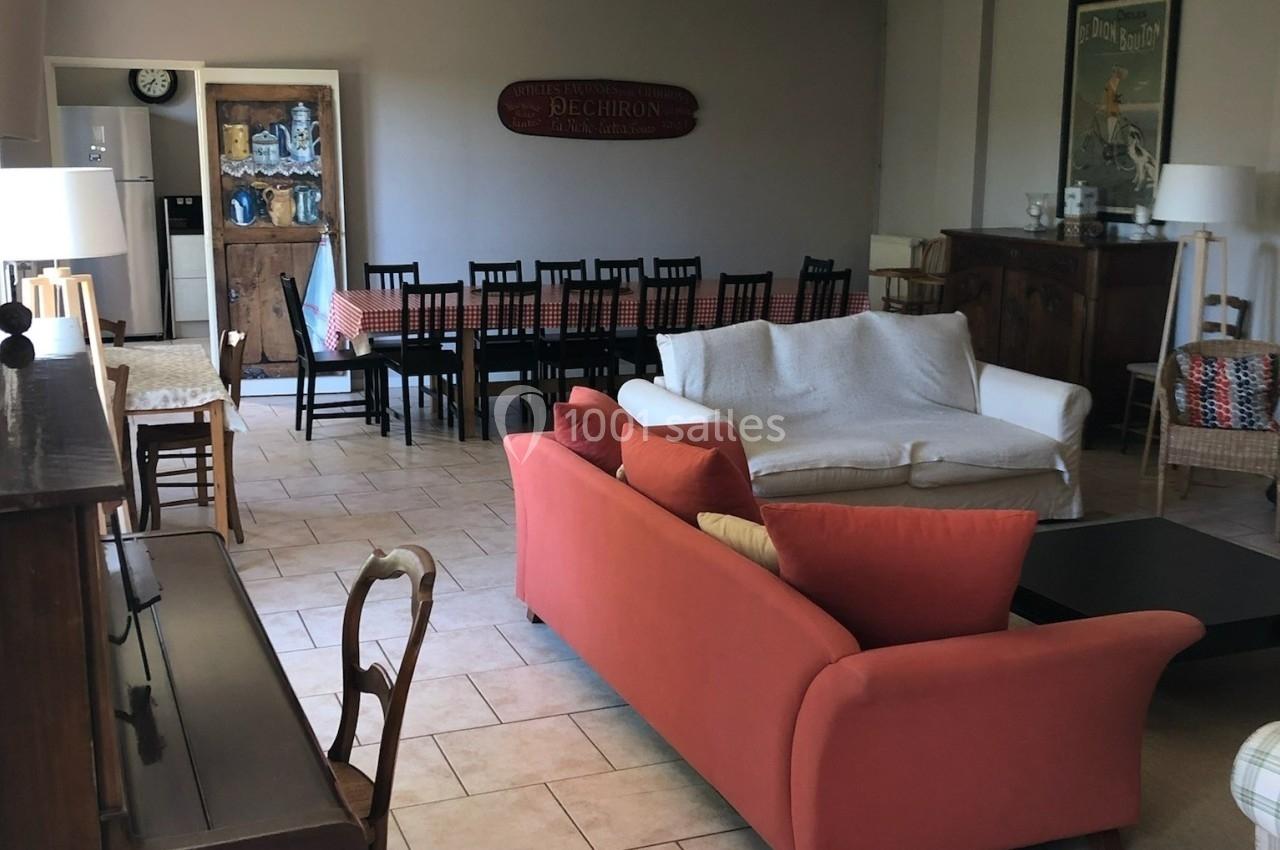 Salon spacieux avec canapés, table à manger longue, chaises noires et décoration murale dans un intérieur lumineux.