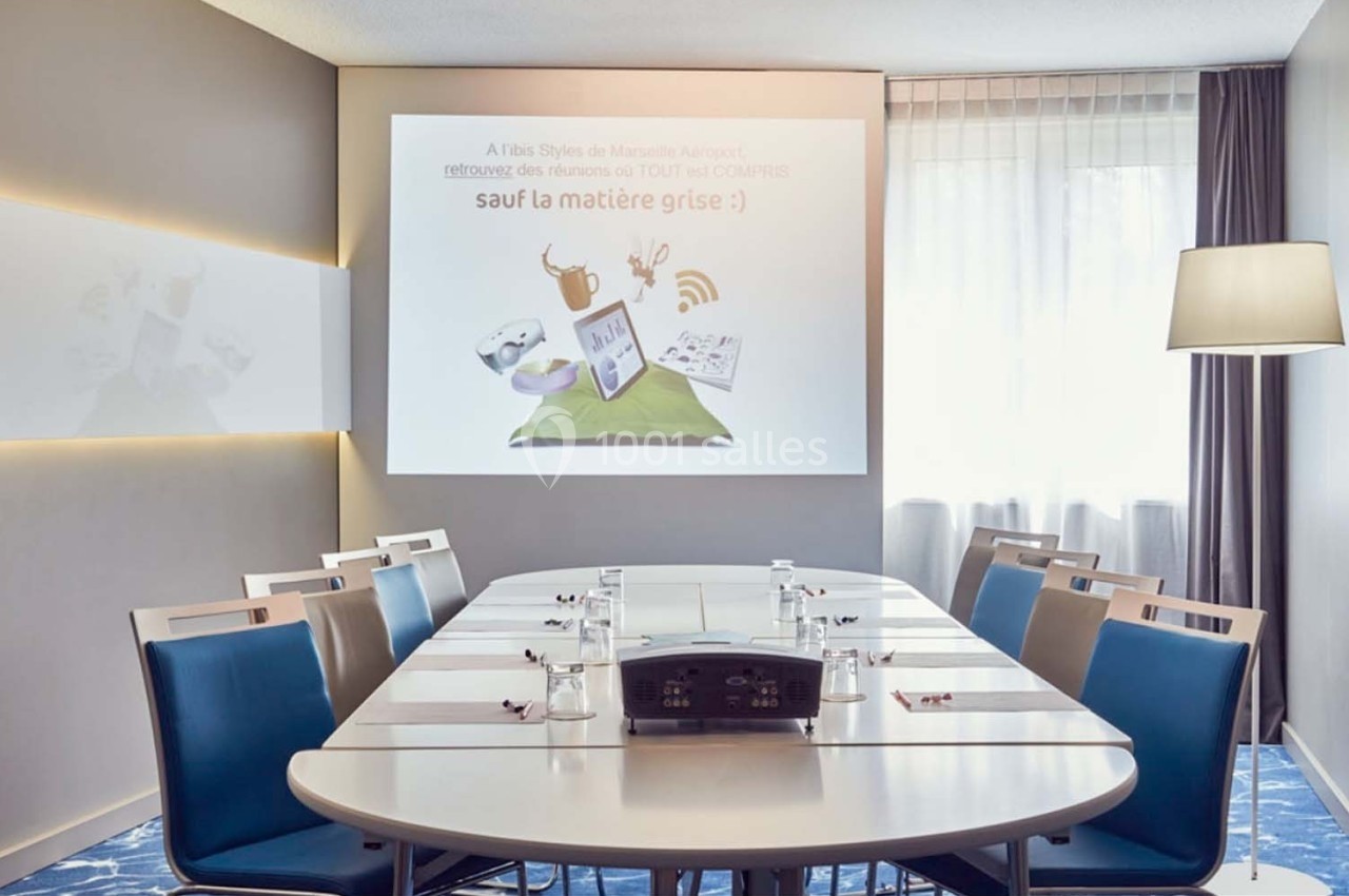 Salle de réunion lumineuse avec une table ovale, chaises modernes et un projecteur affichant une présentation humoristique.