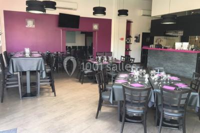 Terrasse en bois avec tables, chaises colorées et parasols verts et rouges, entourée de végétation et de bâtiments.
