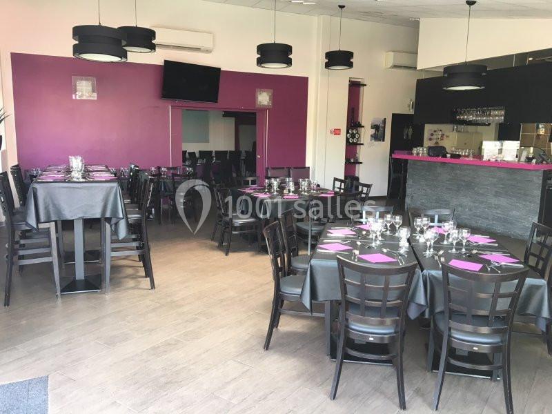 Salle de restaurant moderne avec tables dressées, nappes grises et accents décoratifs violets, bar en arrière-plan.