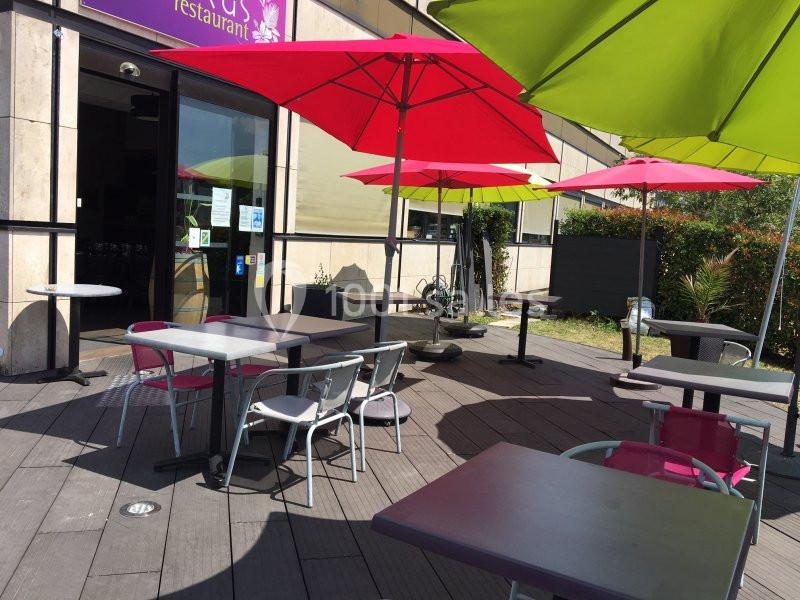 Terrasse d'un restaurant avec des tables, des chaises et des parasols colorés, située devant une entrée vitrée.
