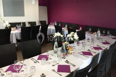 Terrasse en bois avec tables, chaises colorées et parasols verts et rouges, entourée de végétation et de bâtiments.