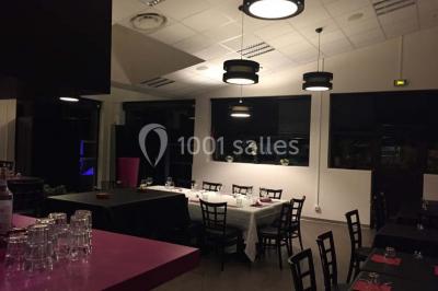 Terrasse en bois avec tables, chaises colorées et parasols verts et rouges, entourée de végétation et de bâtiments.